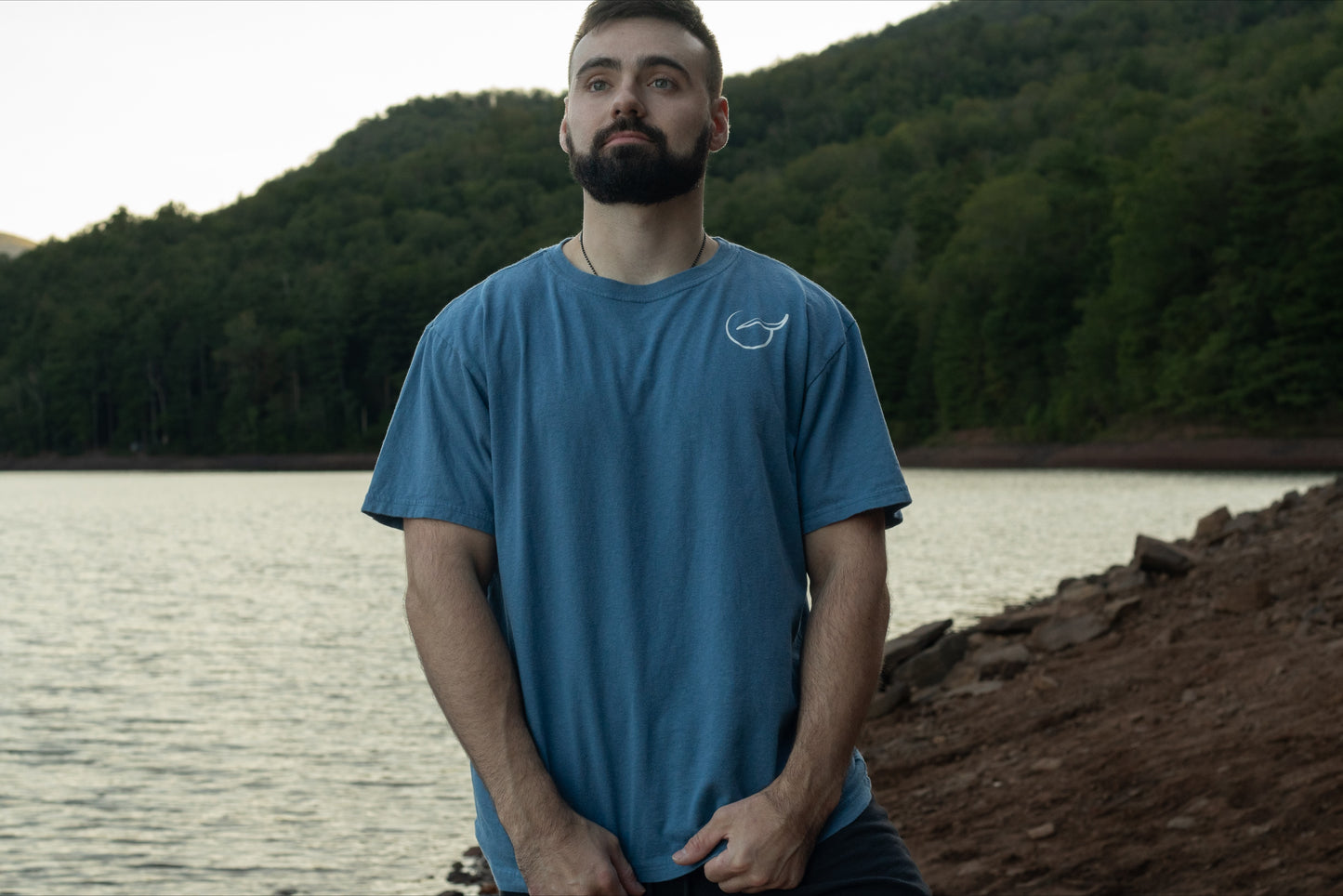 A person displaying the front of the light blue graphic t shirt made with 100% organic cotton with Breath logo on the front left chest.