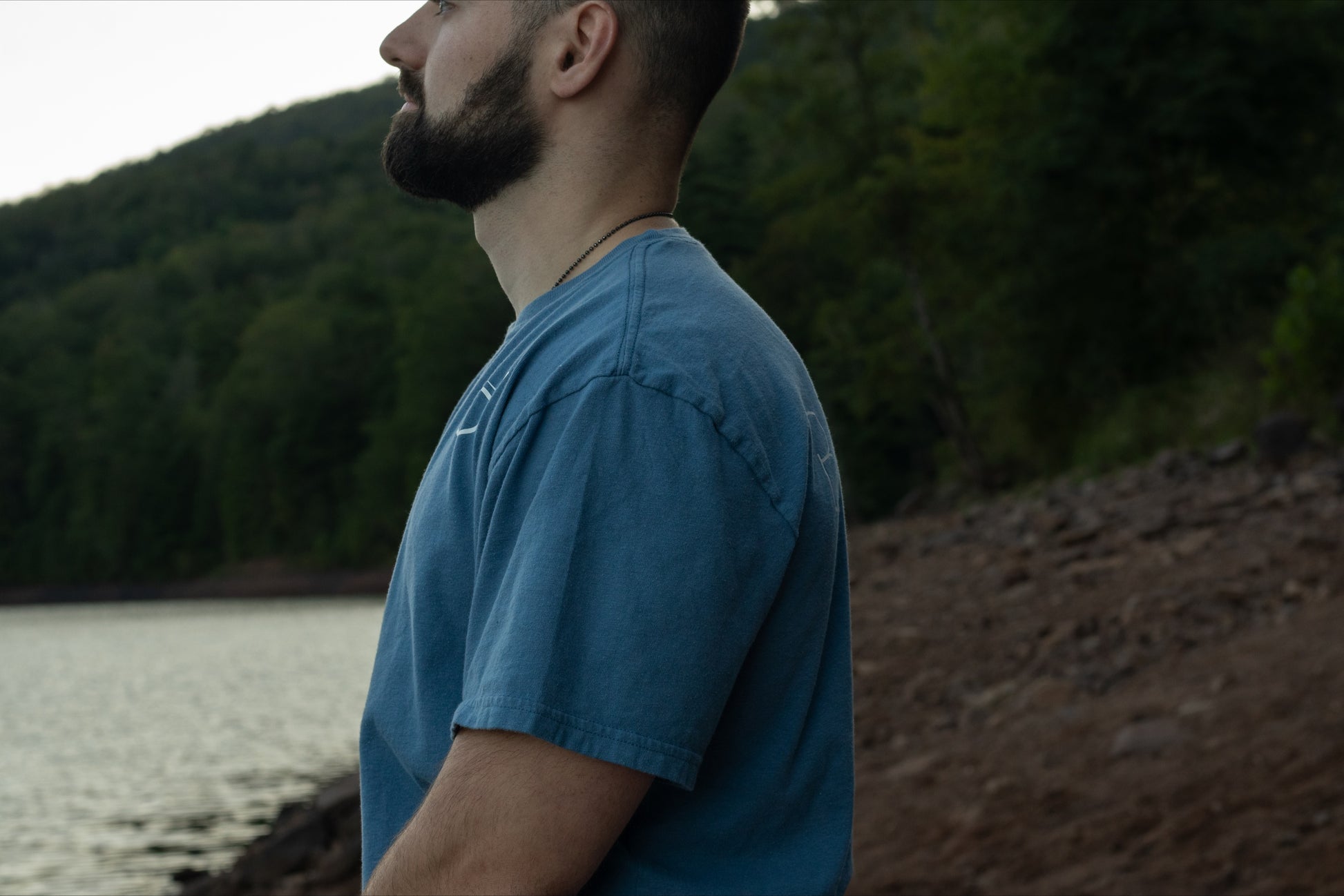 A person showing the drape of the 100% organic cotton light blue t shirt from breath with the logo on the front left chest.