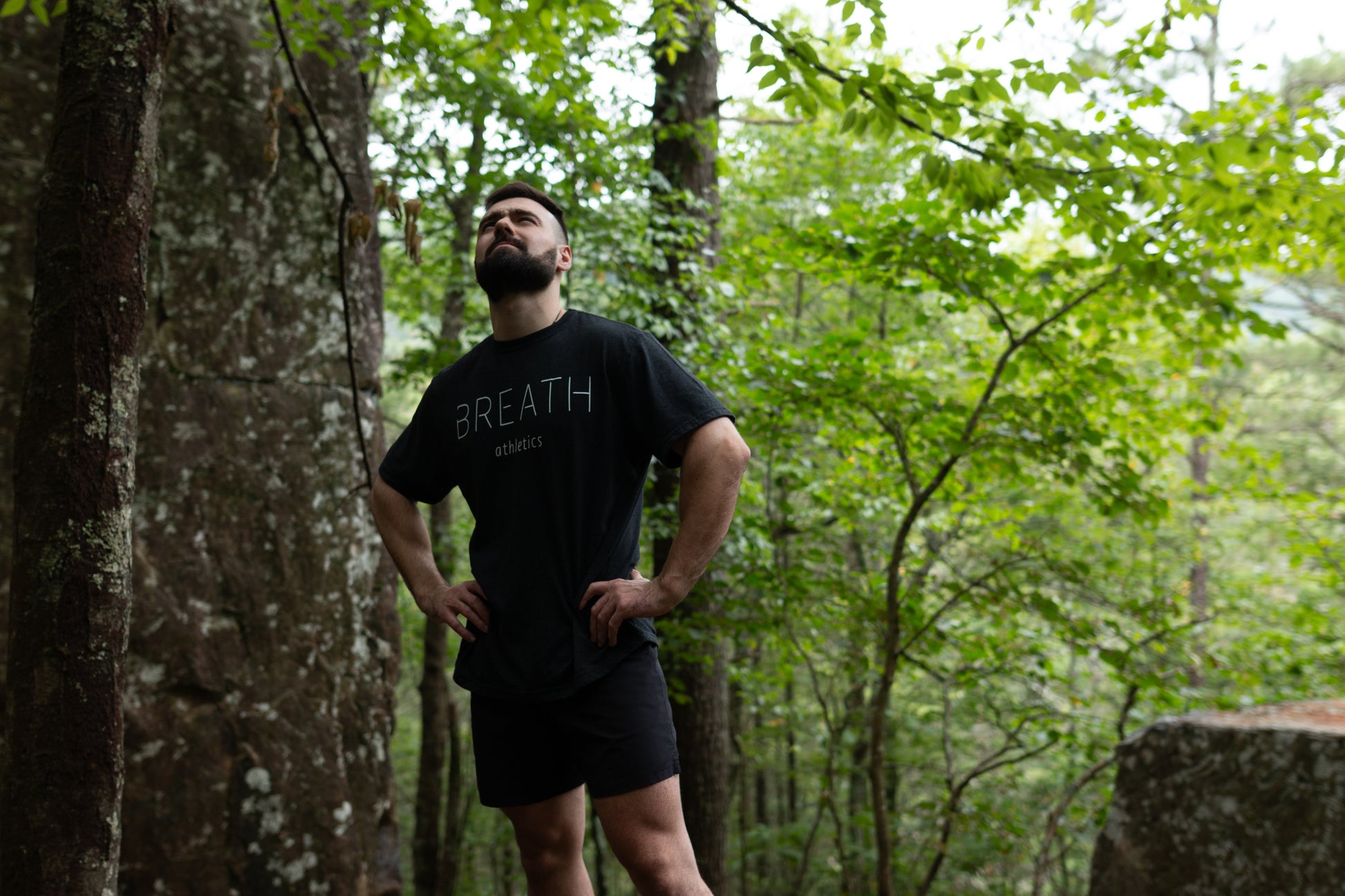 A person displaying the front of the 50/50 blend black short sleeve t shirt by Breath with the brand name across the front and the logo between the shoulder blades.
