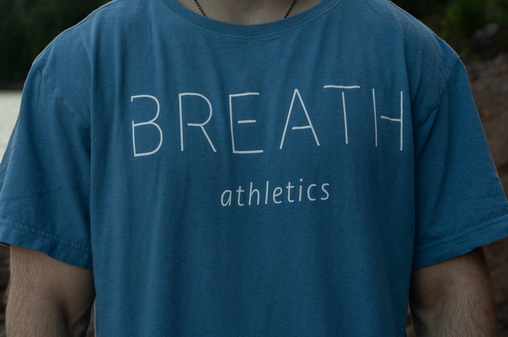 Close up view of the Front of light blue t shirt made from 100% Organic Cotton displaying the Breath brand name across the front with the logo on the back.