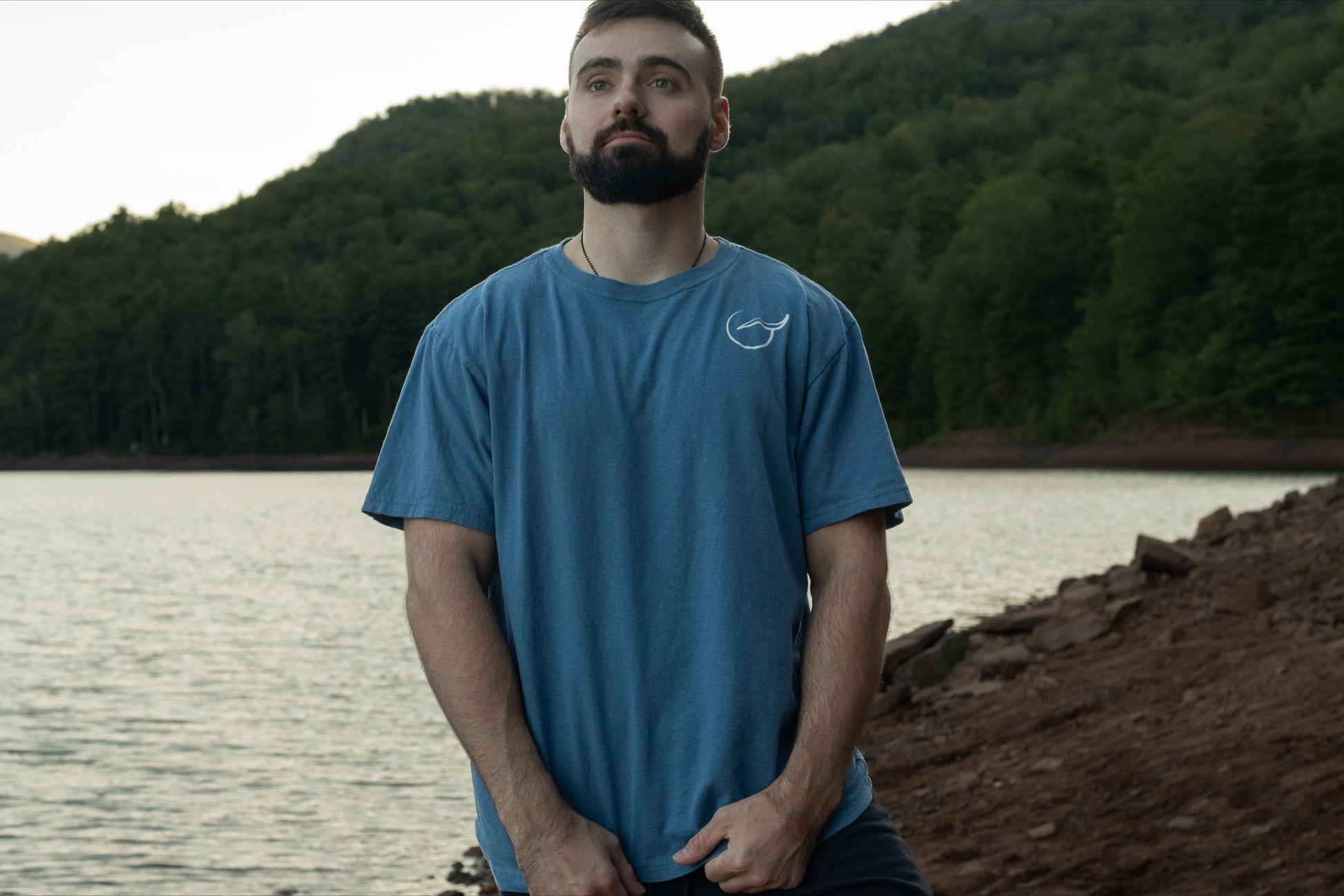 A person displaying the front of the light blue graphic t shirt made with 100% organic cotton with Breath logo on the front left chest.