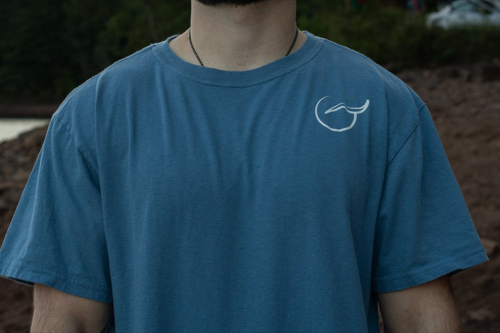 A person displaying the front of the 100% organic cotton light blue graphic t shirt with the logo on the front left chest by breat.