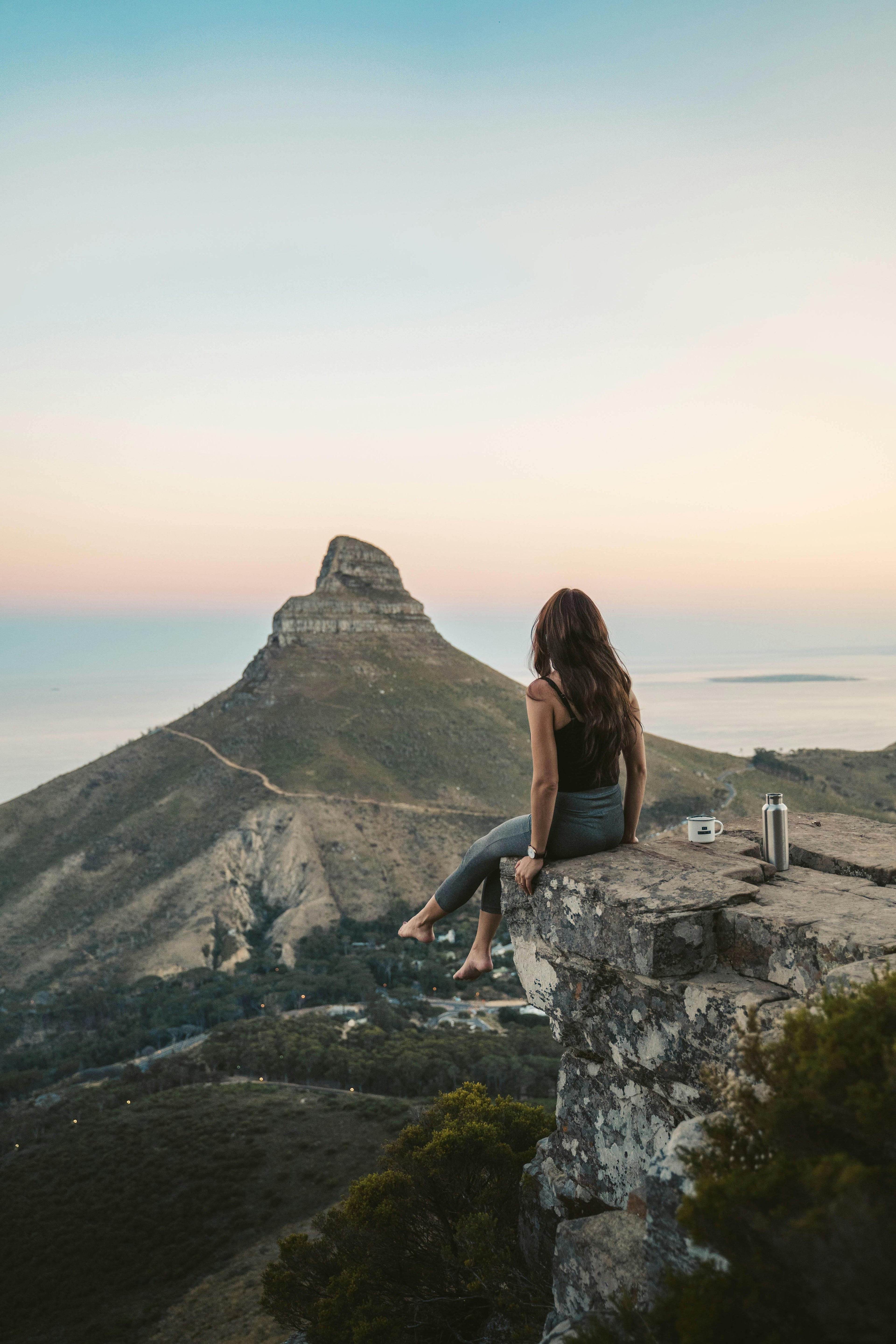 Woman in sustainable activewear sitting peacefully on a mountain at sunset, symbolizing mindful movement and eco-conscious living